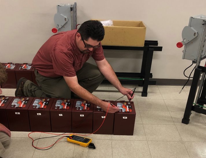 Electrical worker measuring a physical battery bank during procedural training.